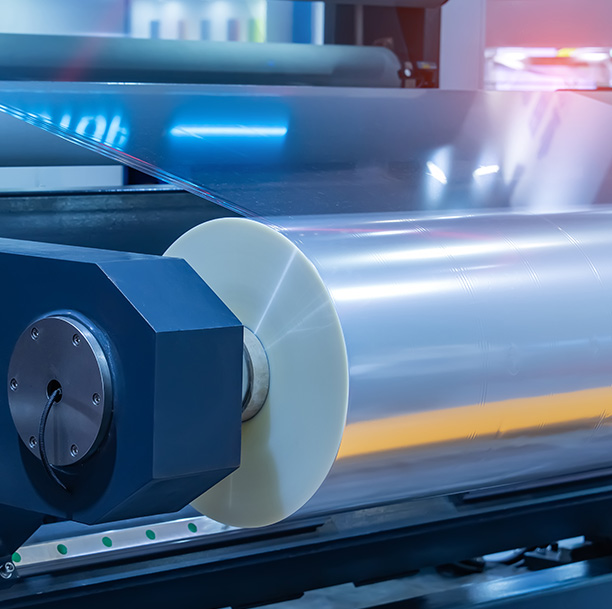 Industrial machinery with a large roll of film in a production environment.
